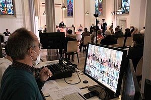 Eröffnungsgottesdienst am Bildschirm Ein Mann sitzt vor einem großen Bildschirm in einer Kirche