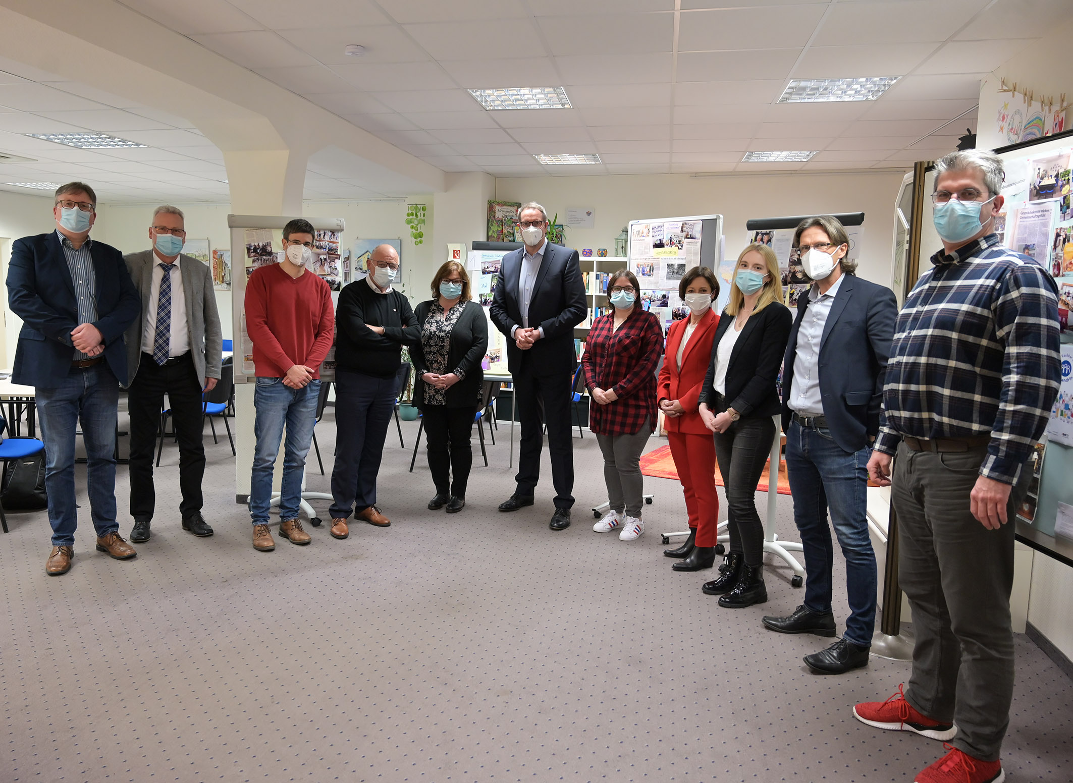 Eine Gruppe Menschen steht in einem Halbkreis im Raum vor Plakatwänden