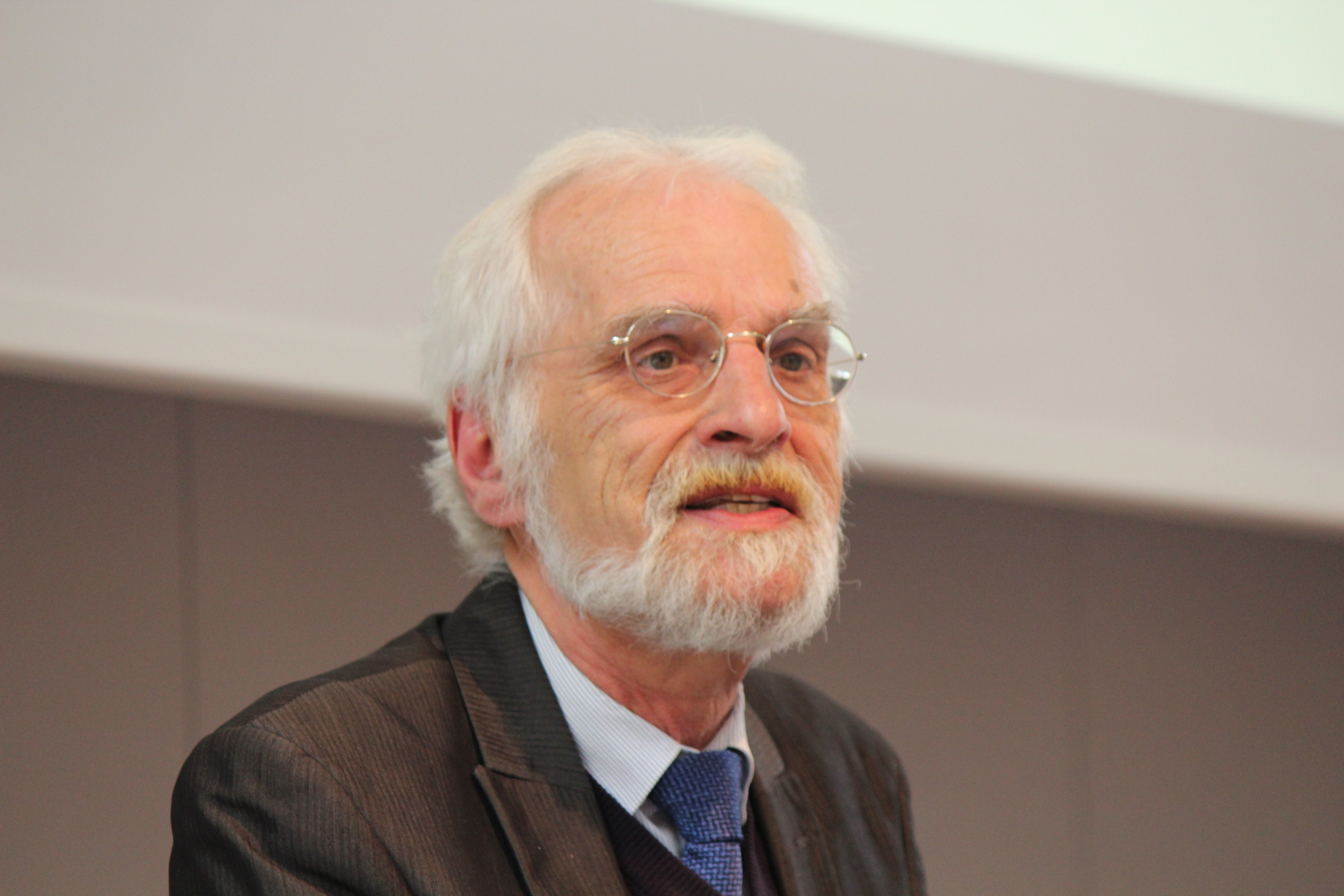 Älterer Mann mit Brille und weißen Haaren an Rednerpult